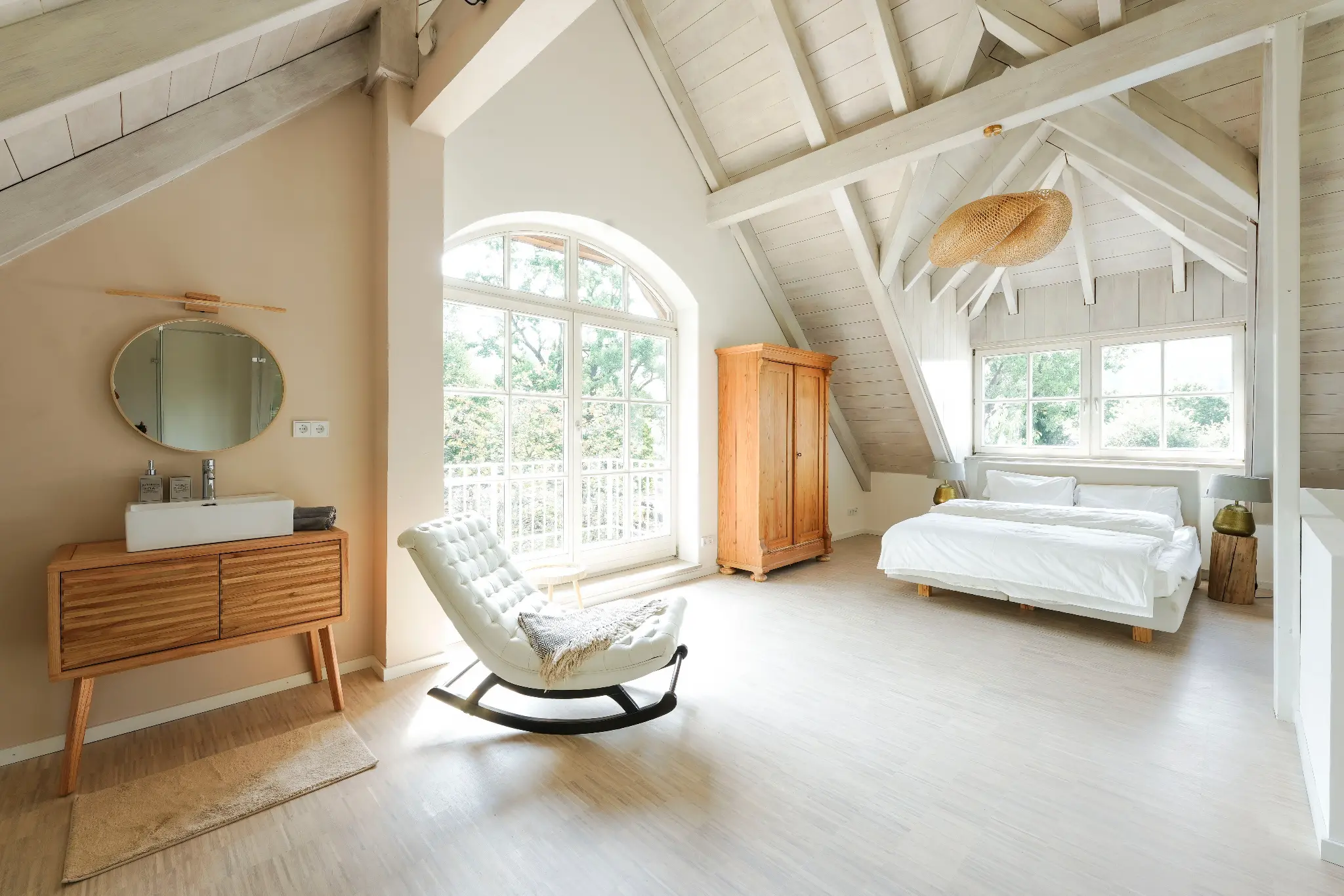 Schlafbereich unter der Dachschräge mit Sideboard, Rundspiegel und Schaukelstuhl am Fenster